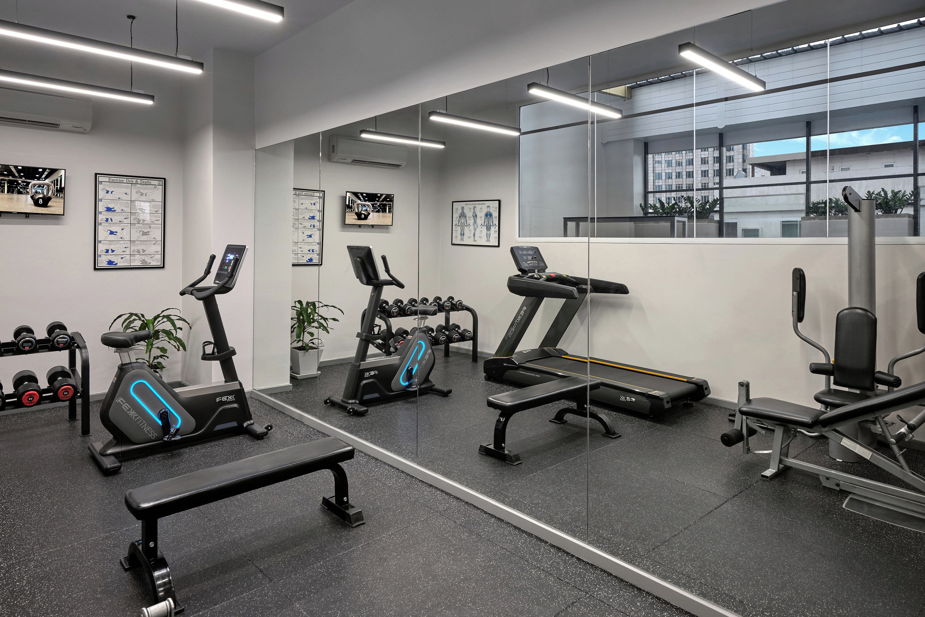 A gym with exercise equipment, a bench, dumbbells, and informational posters on the walls.