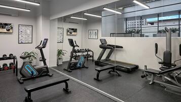 A gym with exercise equipment, a bench, dumbbells, and informational posters on the walls.