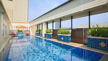 A swimming pool with blue tiles, surrounded by lounge chairs and potted plants.