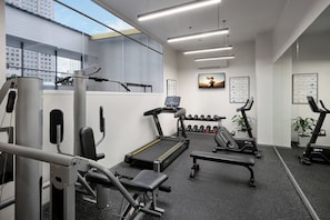 Un gimnasio moderno con equipo de ejercicio, una cinta de correr, mancuernas y un televisor de pared.