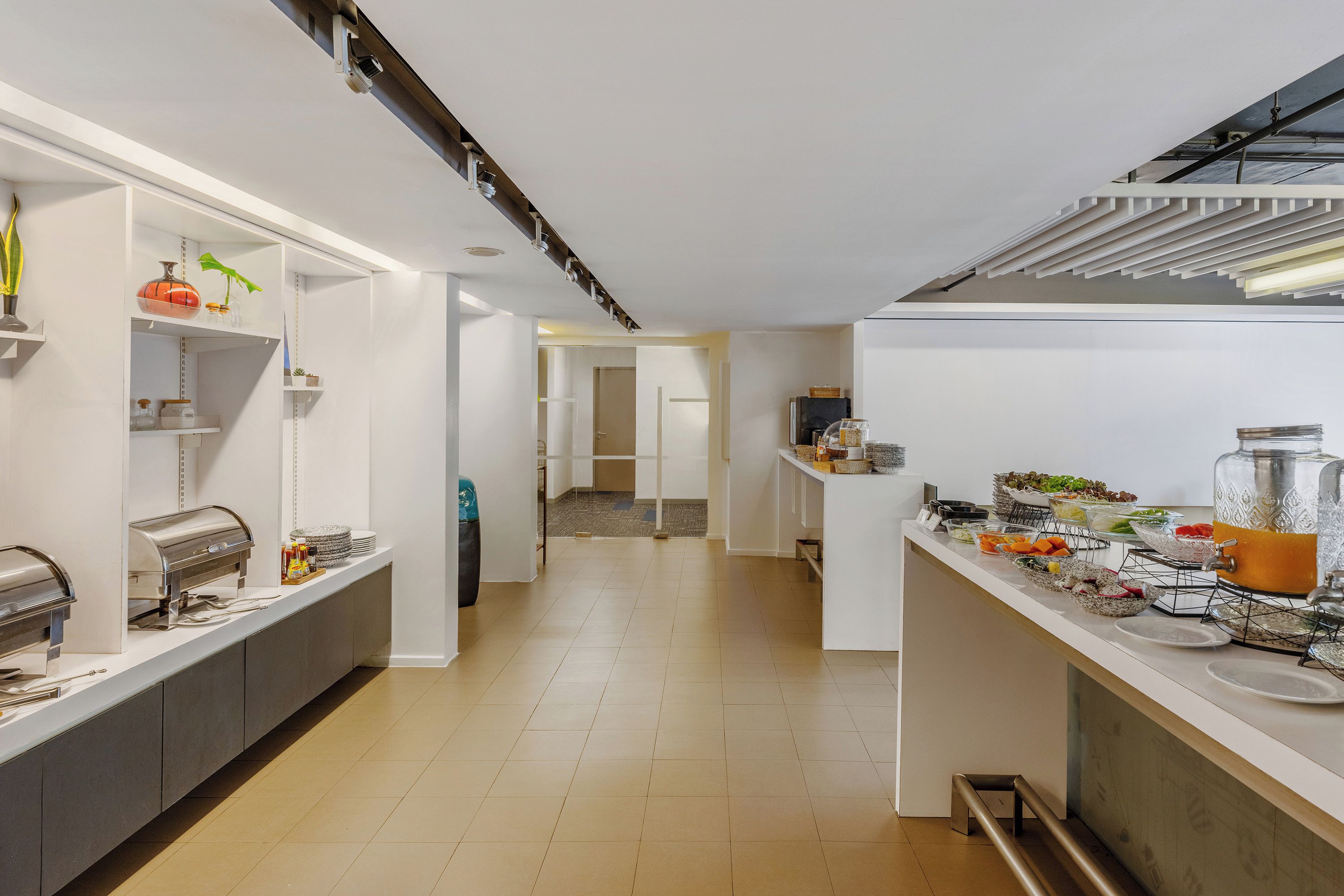 A modern kitchen with a long counter, equipped with a coffee machine, and various food items displayed.