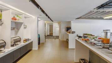 A modern kitchen with a long counter, equipped with a coffee machine, and various food items displayed.