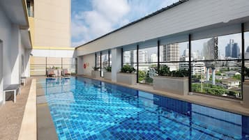 A swimming pool with a city view, surrounded by a building with large windows and a balcony.