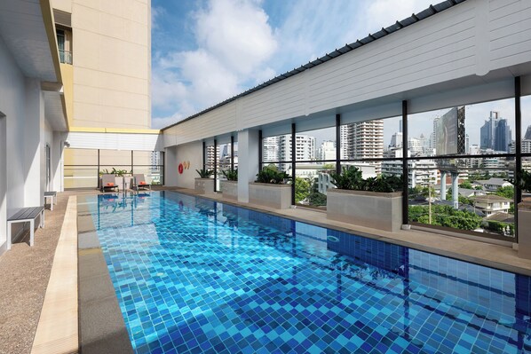 A swimming pool with a city view, surrounded by a building with large windows and a balcony.