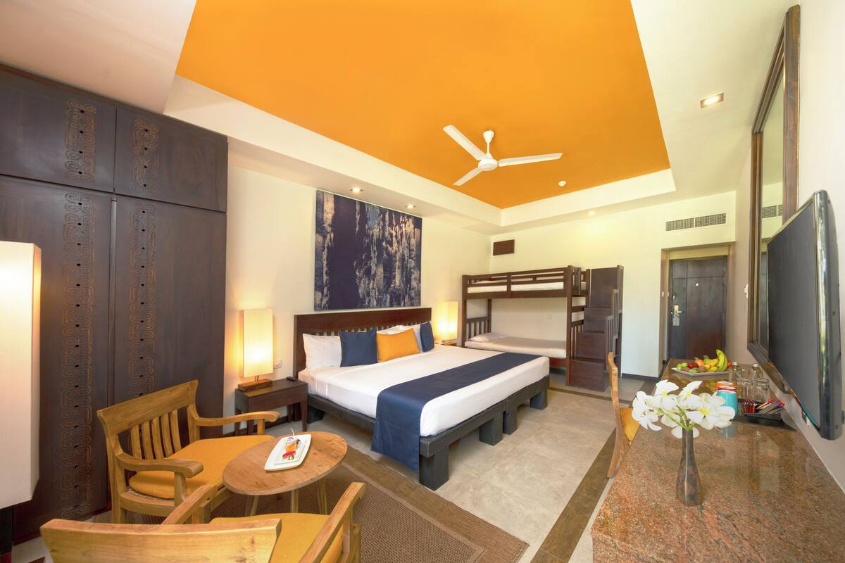 A hotel room with a bed, a desk, a chair, a TV, and a ceiling fan.