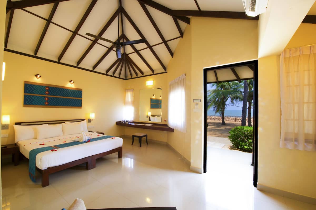 A hotel room with a large bed, a desk, a mirror, and a view of the beach.