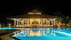 Vista nocturna de un hotel con piscina, zona de estar cubierta al aire libre y estilo arquitectónico tradicional.