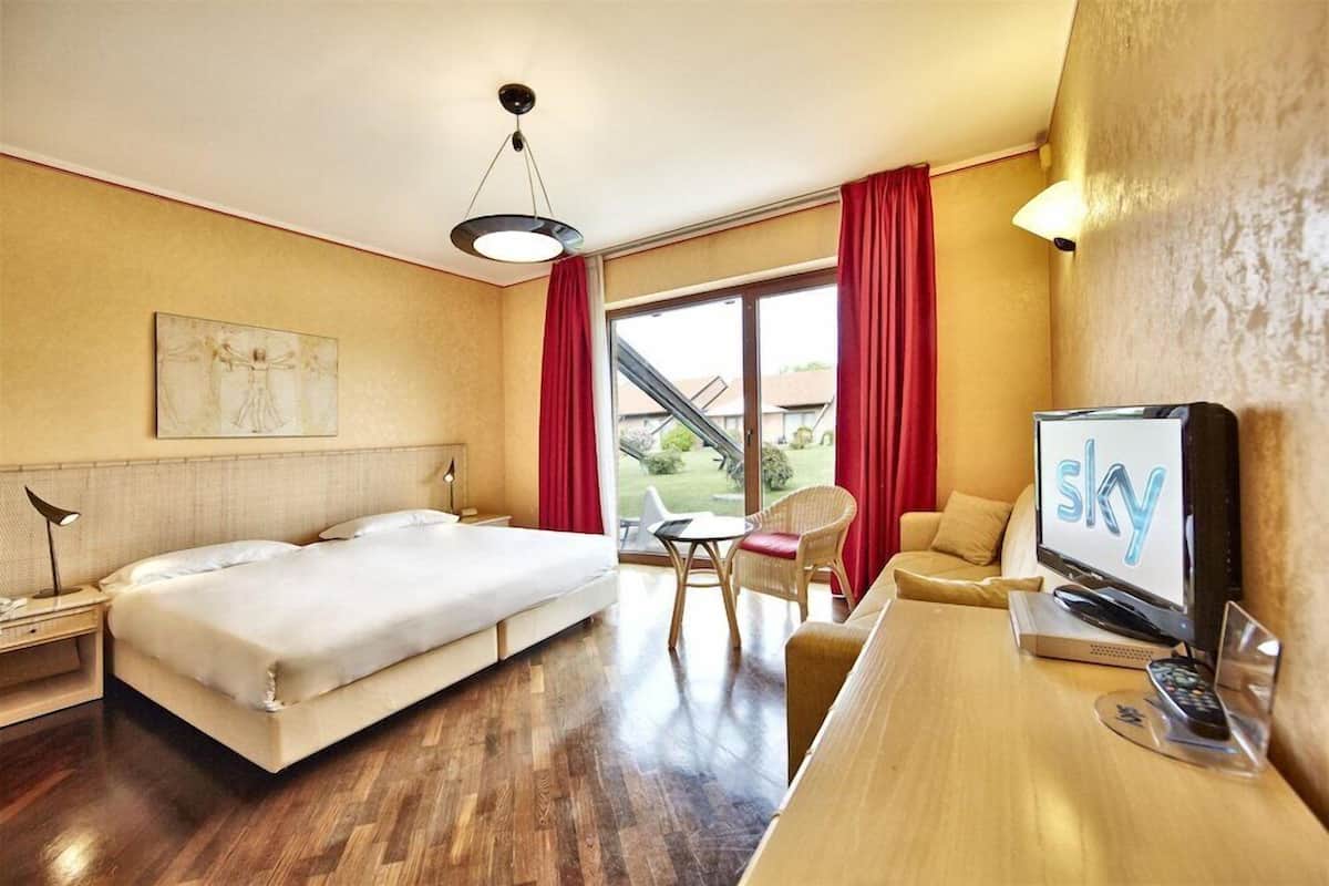 A hotel room with a bed, a desk with a TV, a chair, and a window with curtains.