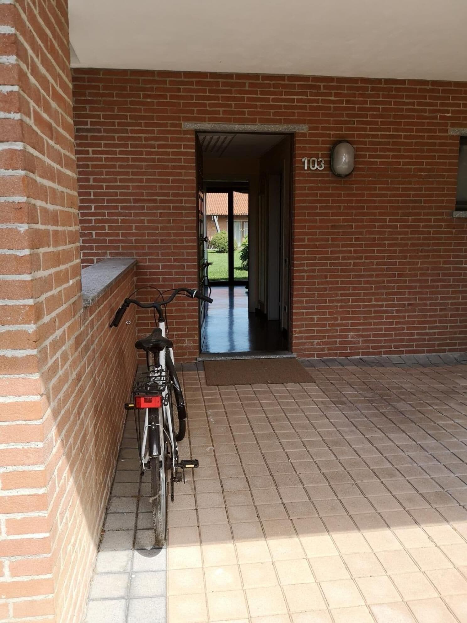 A brick building with a numbered door, a bicycle parked against the wall, and a clear view into the building through an open doorway.