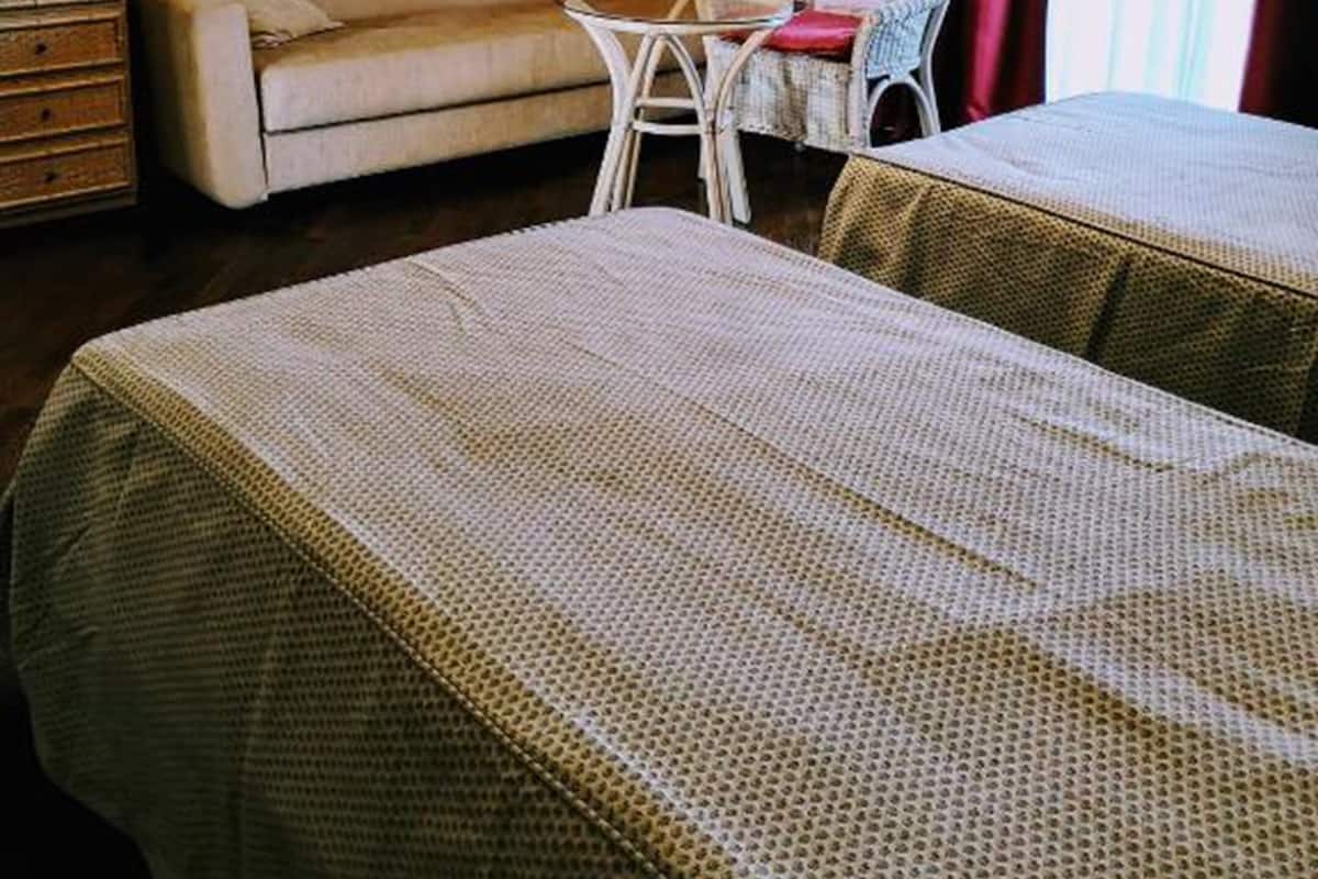 A hotel room with a sofa, two single beds, a small table, a TV, and a window with curtains.