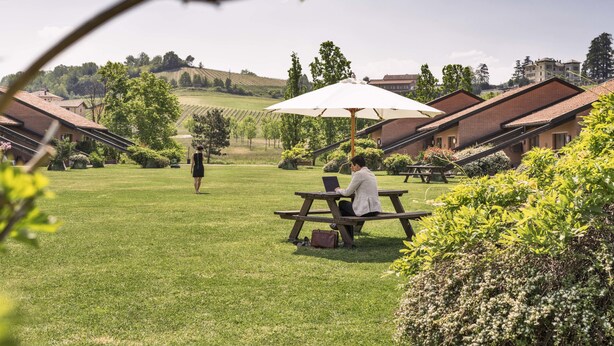 Een binnenplaats met een picknicktafel en parasol, omringd door groen en gebouwen.
