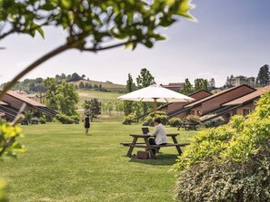 Un patio con mesa de picnic y sombrilla, rodeado de vegetación y edificios.