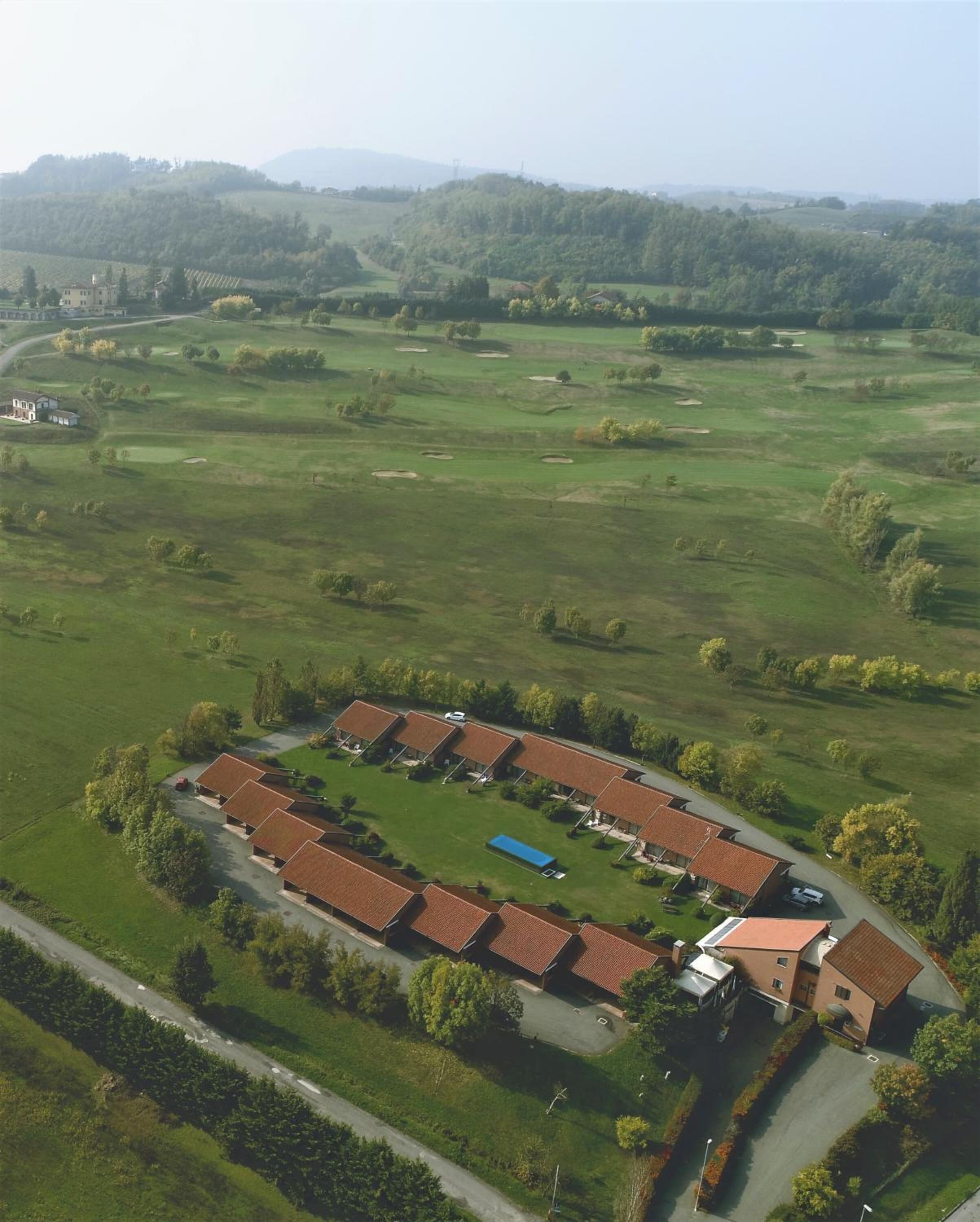 Vista aérea de una propiedad con un amplio campo abierto, varios edificios de techo rojo y algunos árboles.