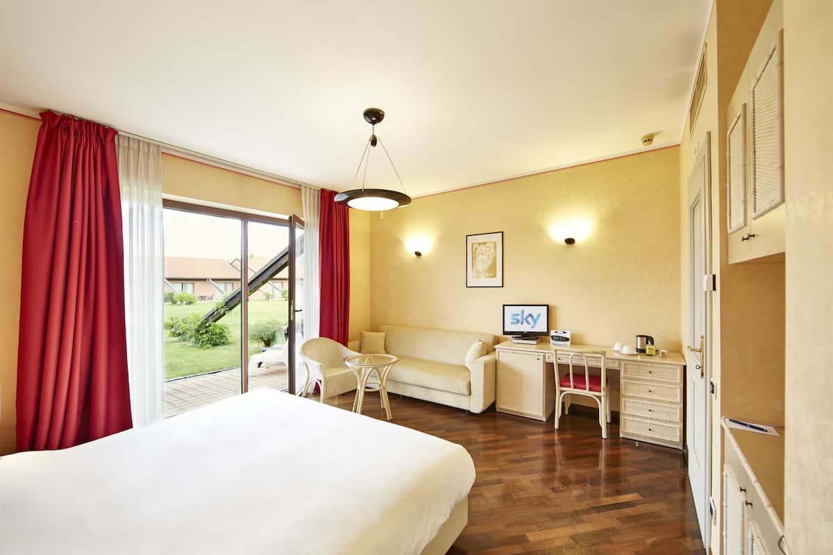 A hotel room with a bed, a desk, a chair, a sofa, and a view of the outdoors.