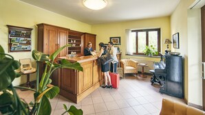 Een hotel lobby met een houten receptiebalie, een prikbord, een groot raam met uitzicht, en een antieke kachel.
