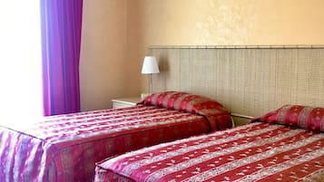 A hotel room with two beds, a nightstand, a lamp, and a window with curtains.