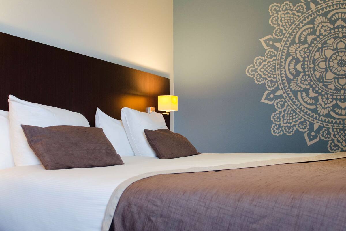 Une chambre d’hôtel avec un lit bien fait, une tête de lit, un mur orné d’un motif décoratif et une lampe de chevet.