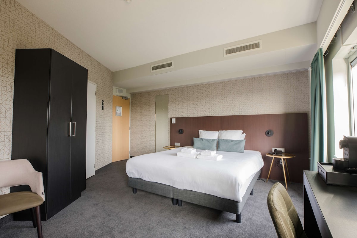 Une chambre d’hôtel avec un grand lit, un bureau, une chaise, une armoire et une petite table.