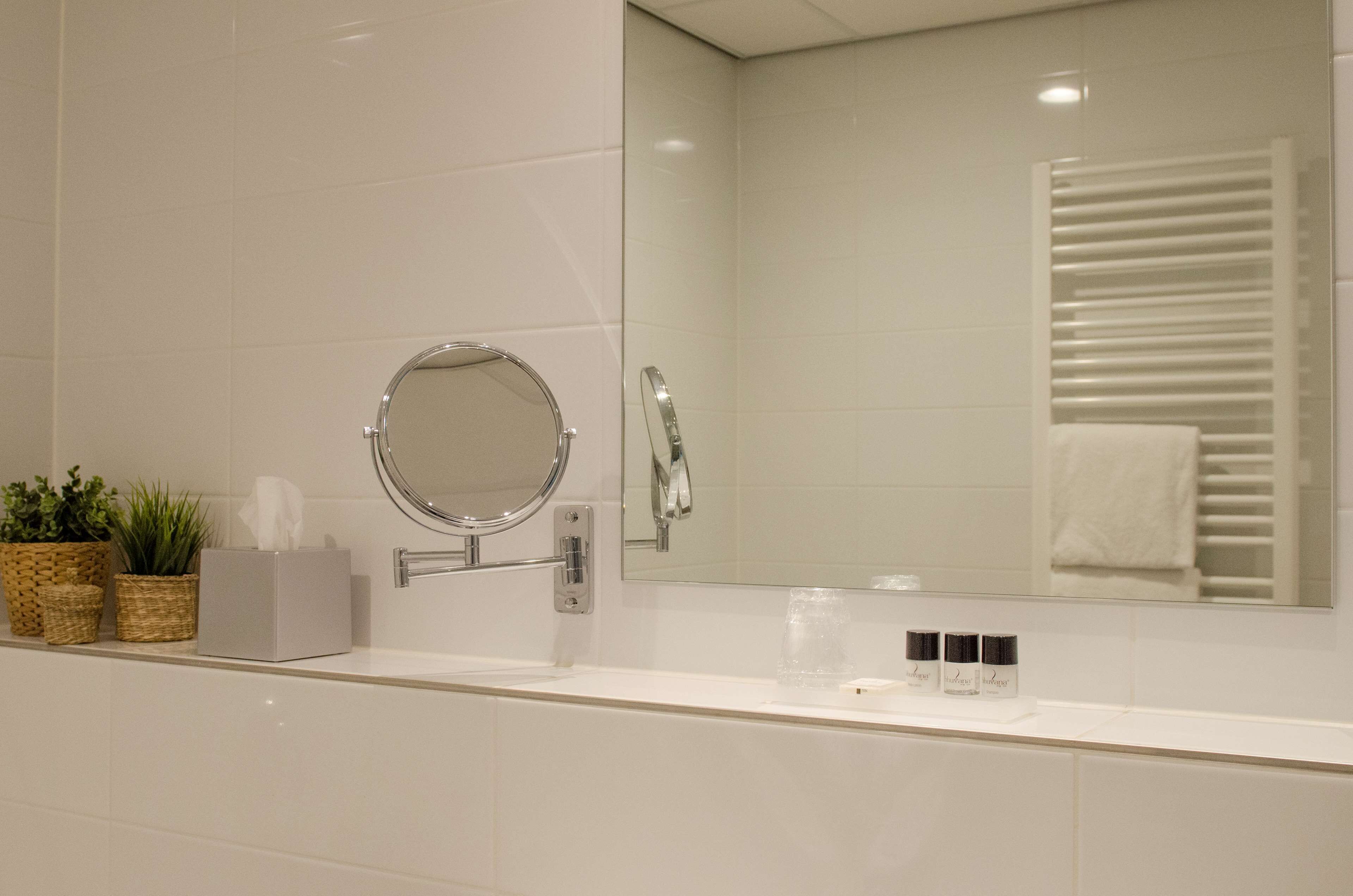 Un baño con tocador blanco, espejo redondo, toallero y dos macetas.