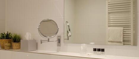 A bathroom with a white vanity, a round mirror, a towel rack, and two potted plants.