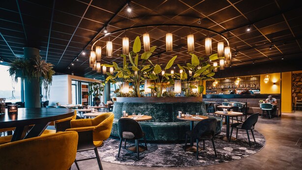 Un área de estar moderna con una planta central, mesas redondas y sillones.