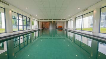 Una piscina interior llarga i estreta, amb parets de vidre transparent i un paviment de rajoles.