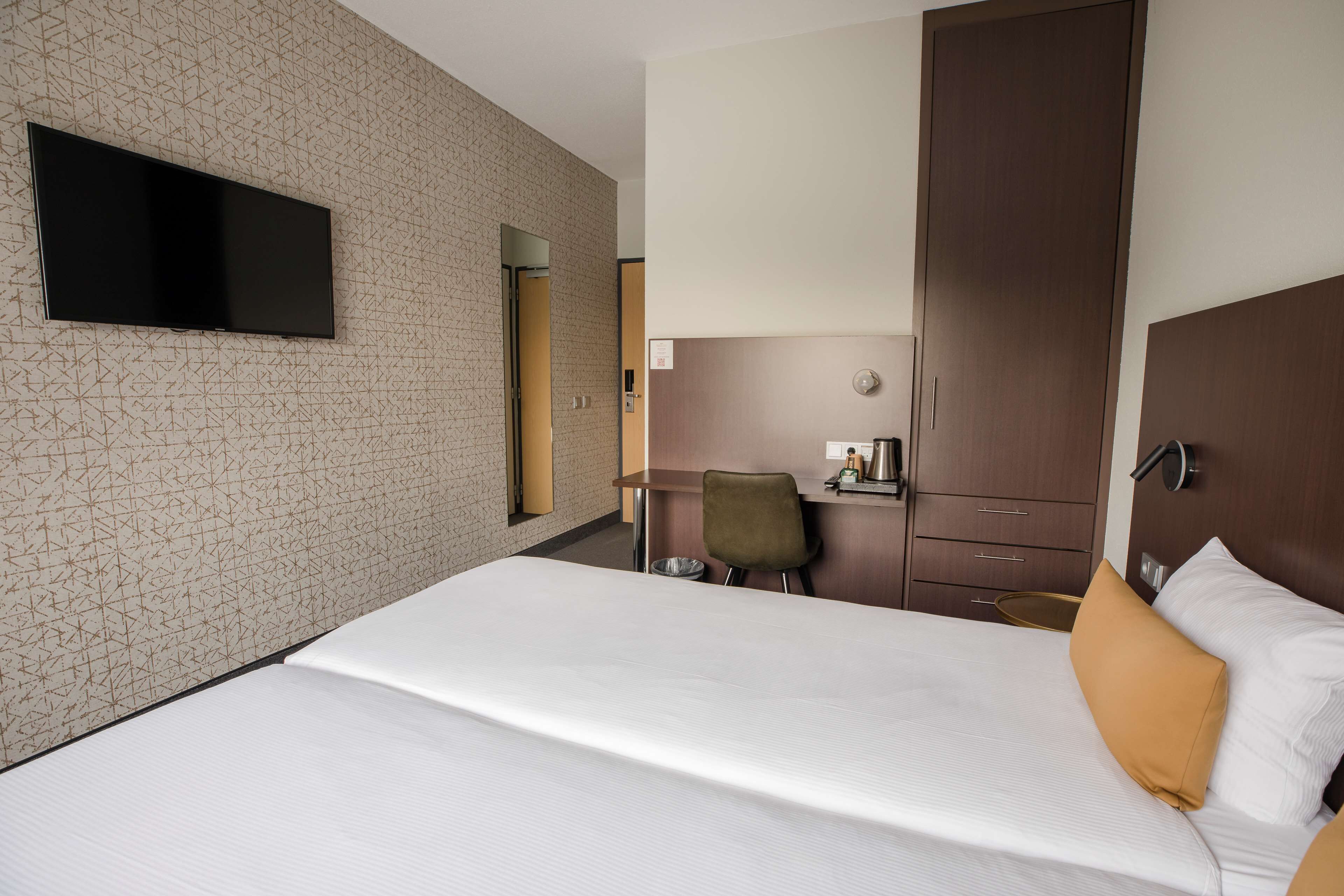 Une chambre d’hôtel avec un grand lit, un téléviseur fixé au mur, une armoire et un bureau avec une chaise.