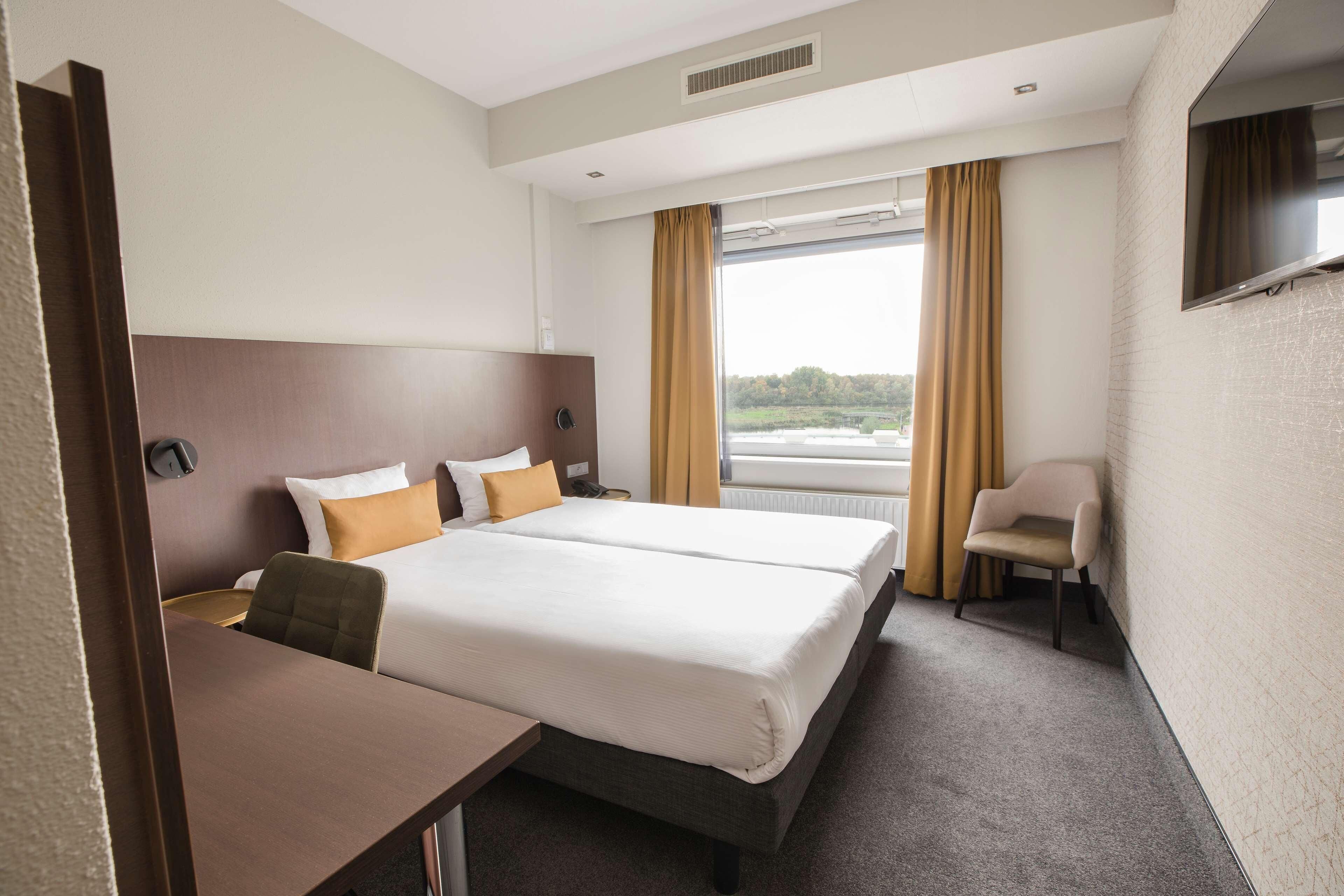 A hotel room with two beds, a desk, a chair, a TV, and a window with curtains.