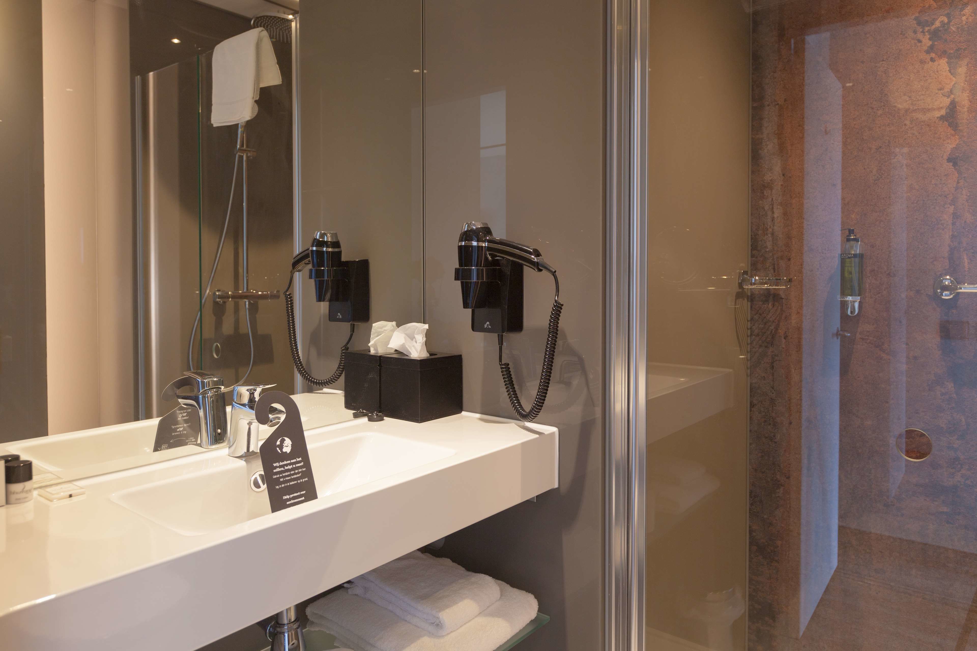 Een moderne badkamer met een douchecabine van glas, een witte wastafel met spiegel, en een haardroger aan de muur.