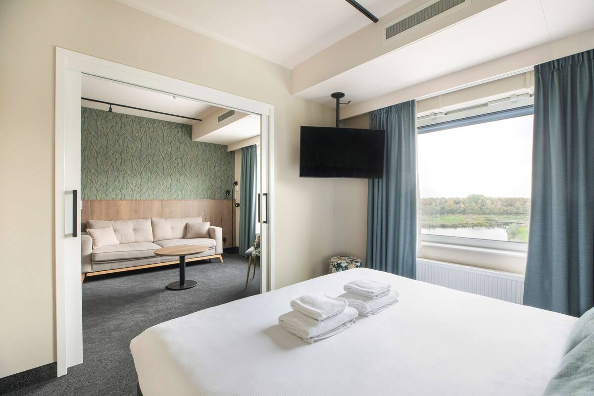 Une chambre d’hôtel avec un grand lit, un téléviseur à écran plat, un canapé et une vue sur un lac.