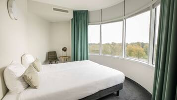 Una habitación de hotel con una cama grande, una mesita y vistas a árboles por la ventana.