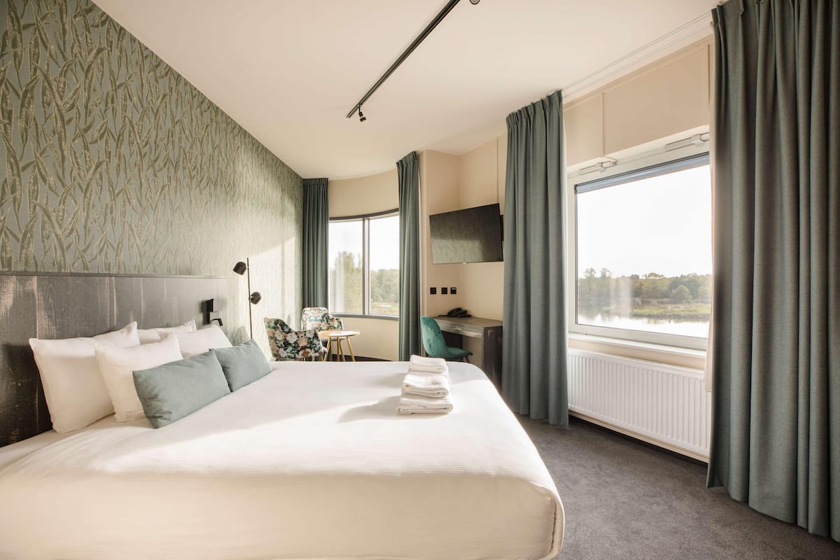 A hotel room with a large bed, a desk, a chair, and a view of a lake.