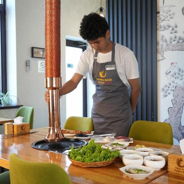 Una persona en una cocina preparando alimentos, con una olla de cobre, una cesta de vegetales verdes y varios recipientes sobre la encimera.