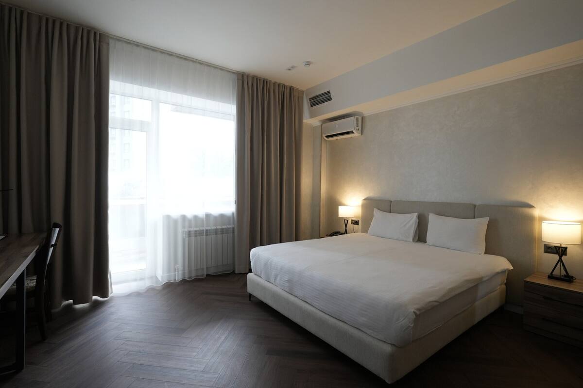 A hotel room with a large bed, two bedside tables with lamps, a desk, and a chair.