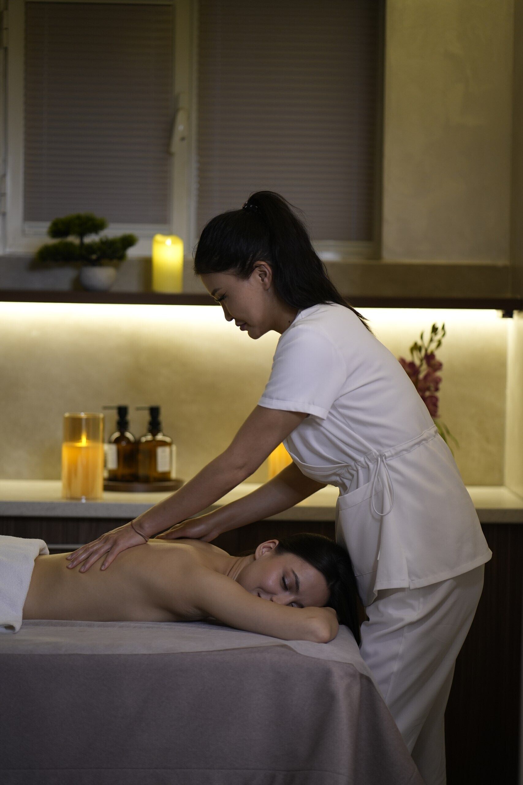 Sesión de terapia de masajes en un entorno de spa, con una camilla, velas y una pequeña planta de fondo.