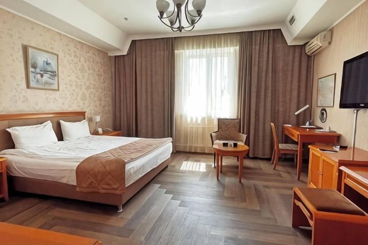 A hotel room with a large bed, a desk, a chair, a TV, and a window with curtains.