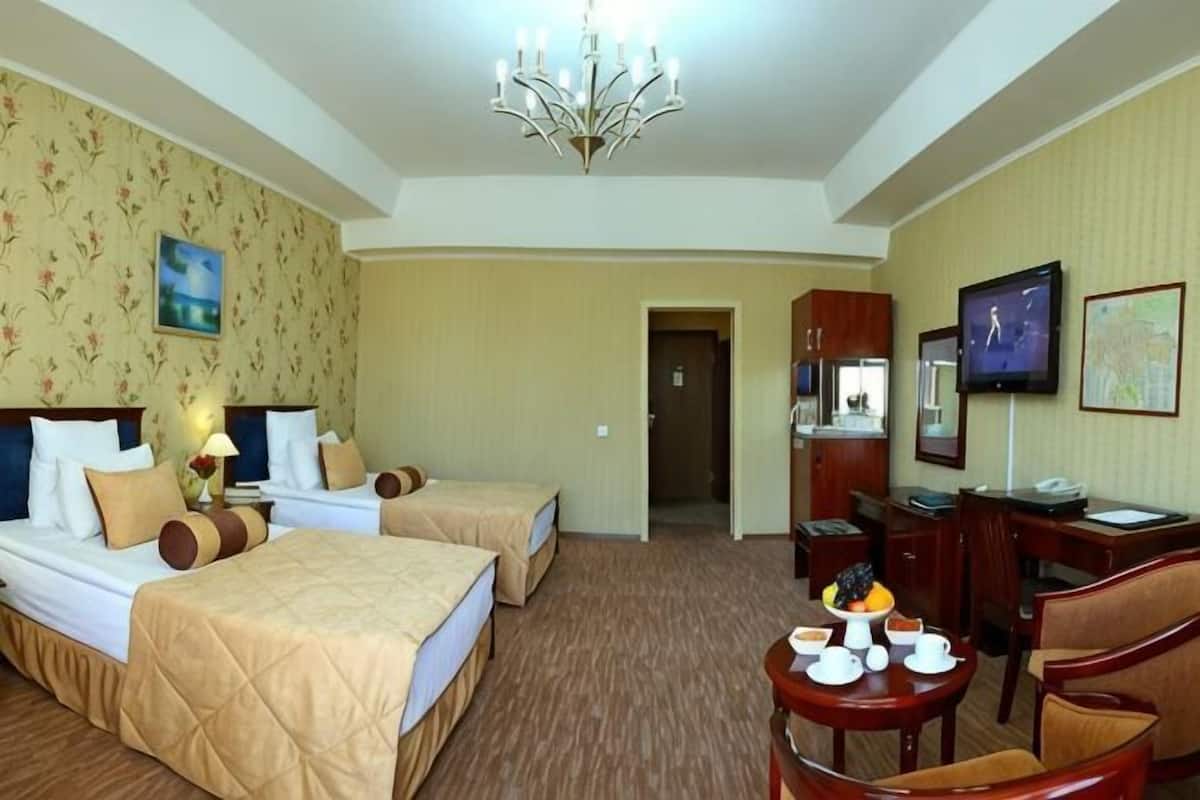 A hotel room with two beds, a desk, a chair, a television, and a chandelier.