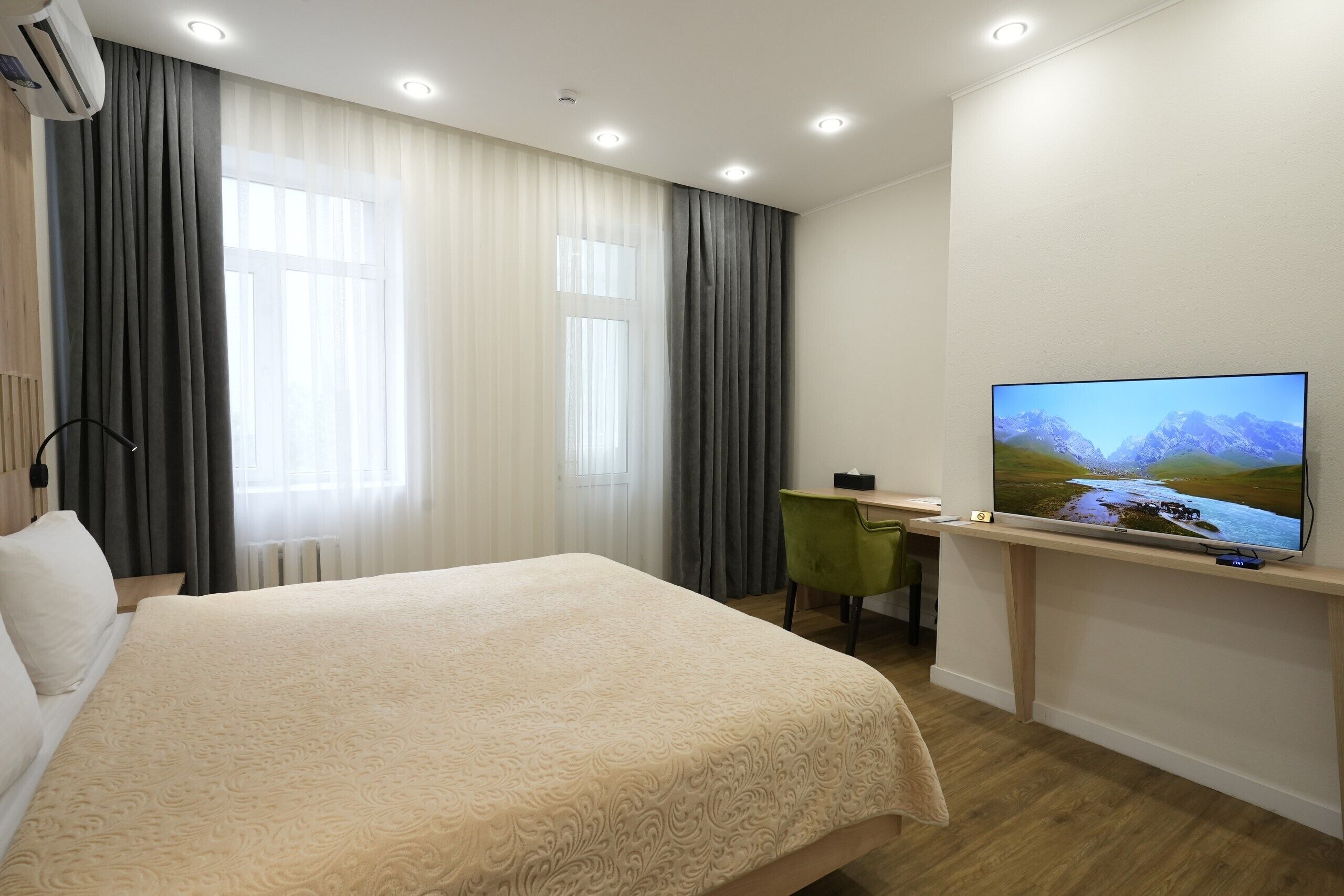 A hotel room with a bed, a desk with a chair, a television, and a window with curtains.