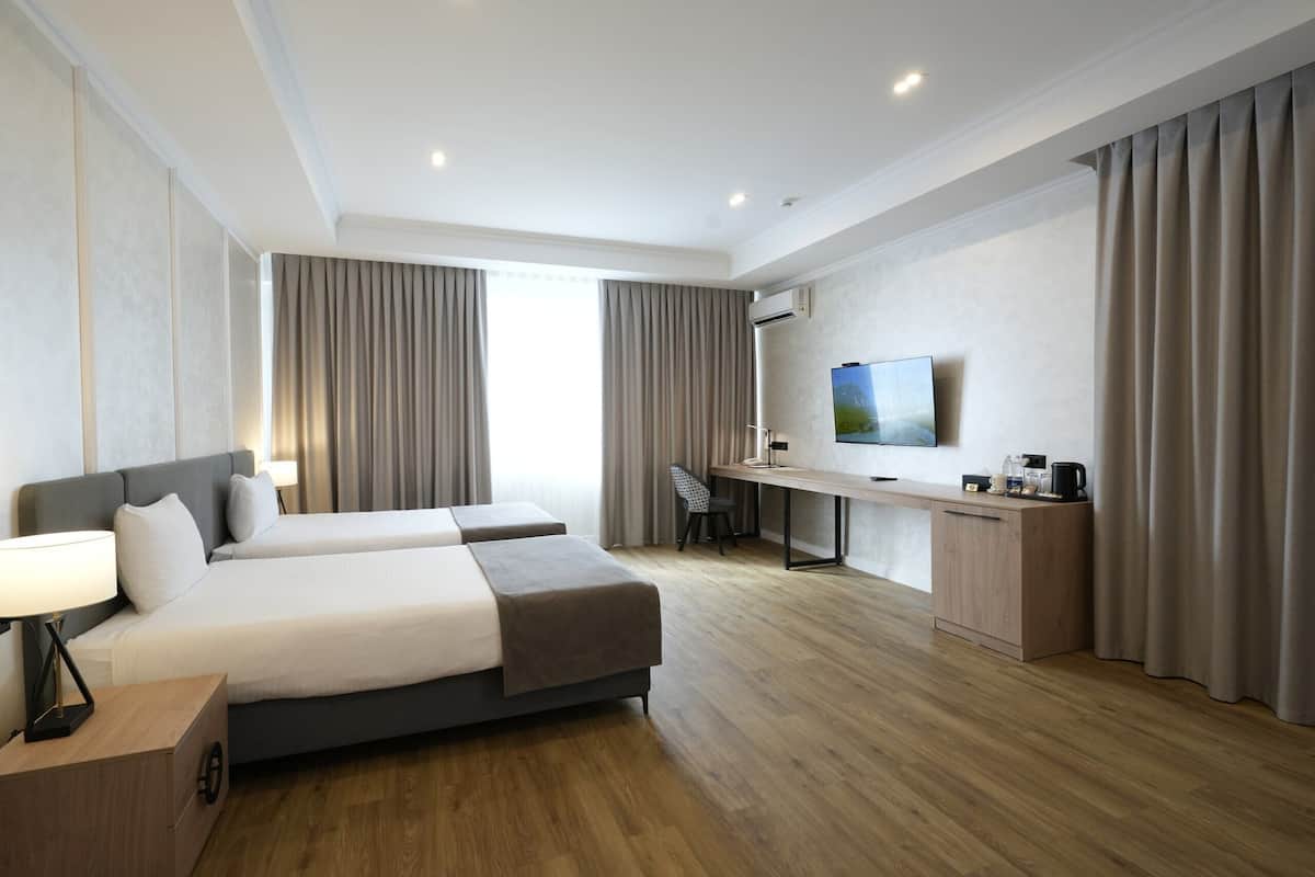 A hotel room with two beds, a desk, a TV, and a window with curtains.