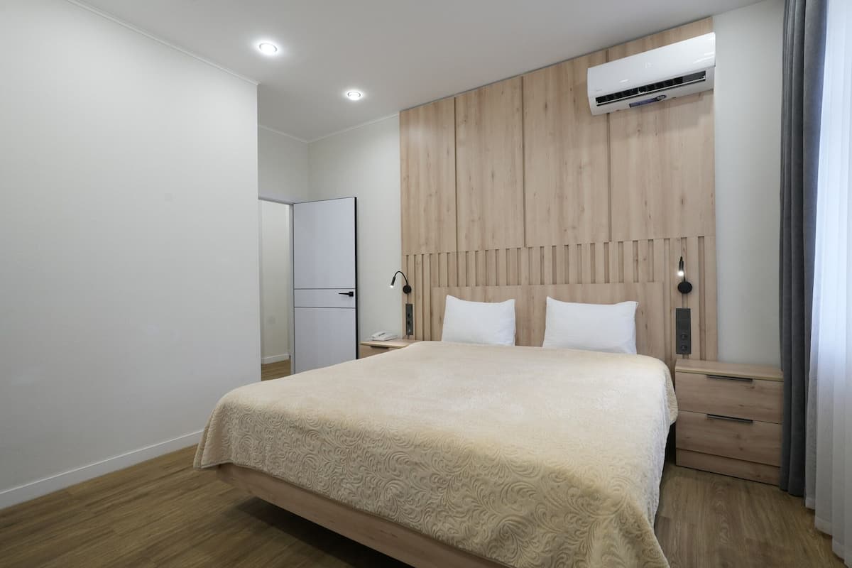 A bedroom with a bed, wooden headboard, bedside tables, a nightstand, an air conditioner, and a door.