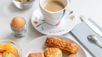 Une table mise pour le petit-déjeuner avec des croissants, une tasse de café et un bol de fruits.