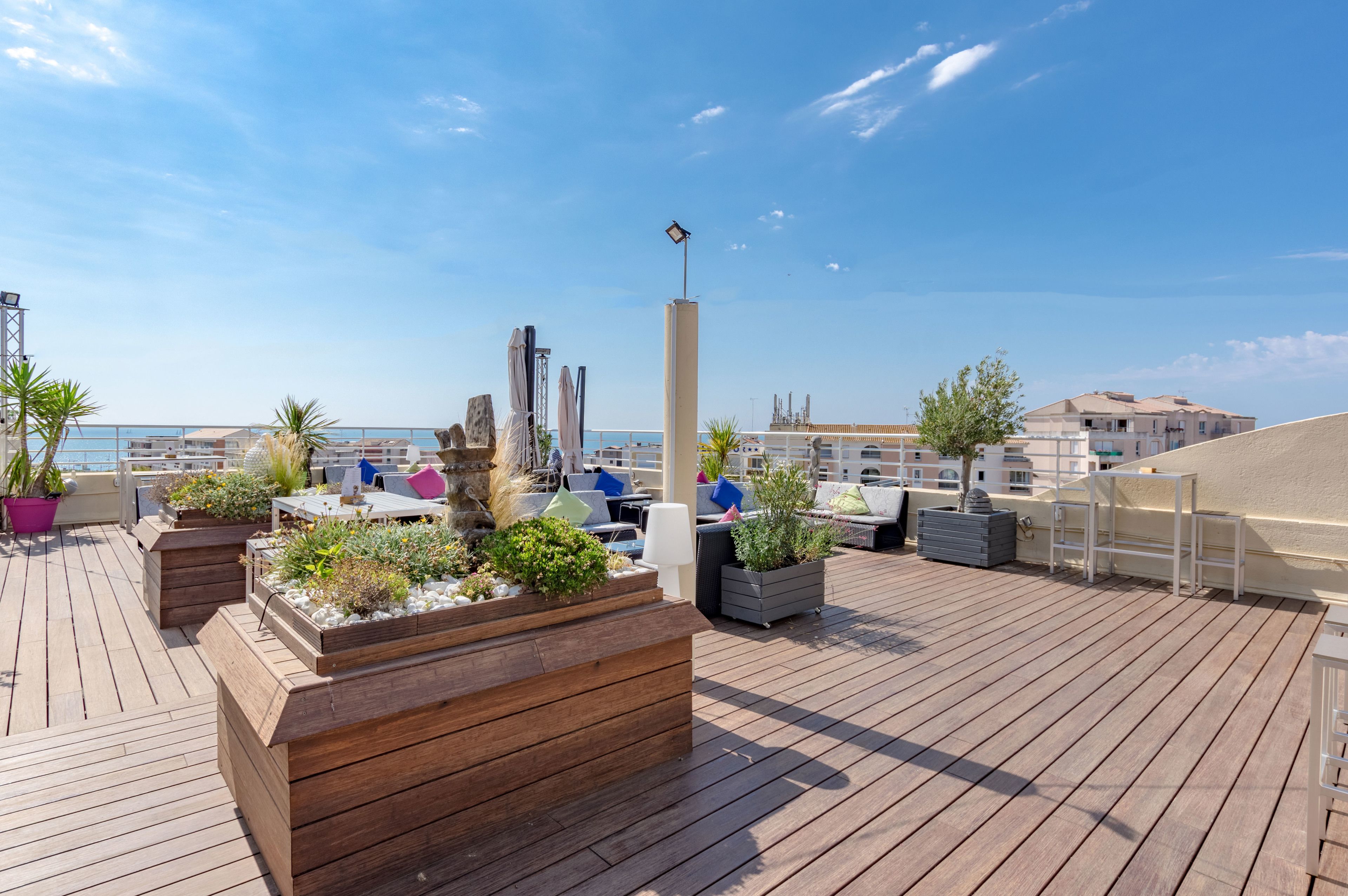 A wooden deck with planters and seating areas, overlooking a body of water and buildings.