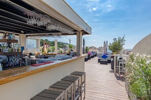 An outdoor bar area with a wooden deck, bar counter, and seating. - Hôtel Impérial (Sète)