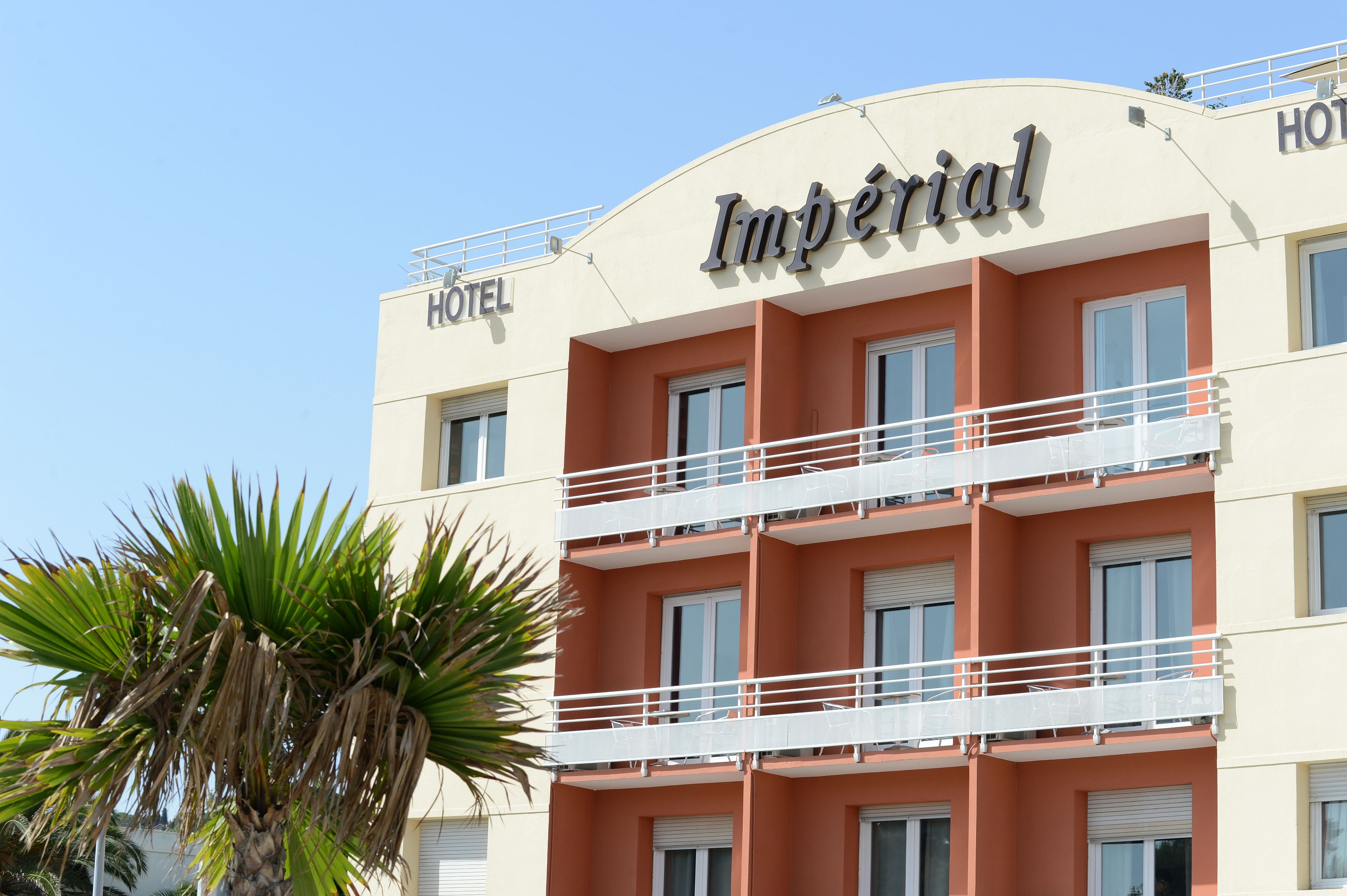 A hotel named "Imperial" with a two-story structure, balconies, and a palm tree in the foreground.