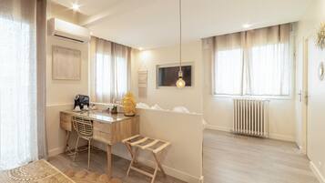 Una habitación moderna y luminosa con un escritorio de madera, una silla, un taburete pequeño, una estatua de Buda y un radiador.