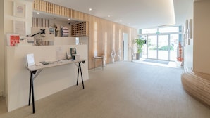 A modern reception area with a reception desk, framed certificates, and a wooden slatted wall. - Hôtel Impérial (Sète)
