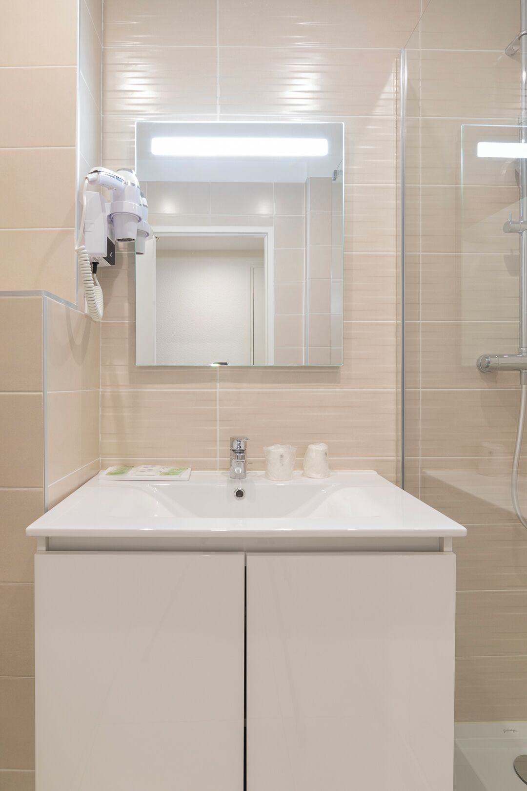Un bagno con un lavandino bianco, uno specchio e un asciugacapelli portatile fissato alla parete.