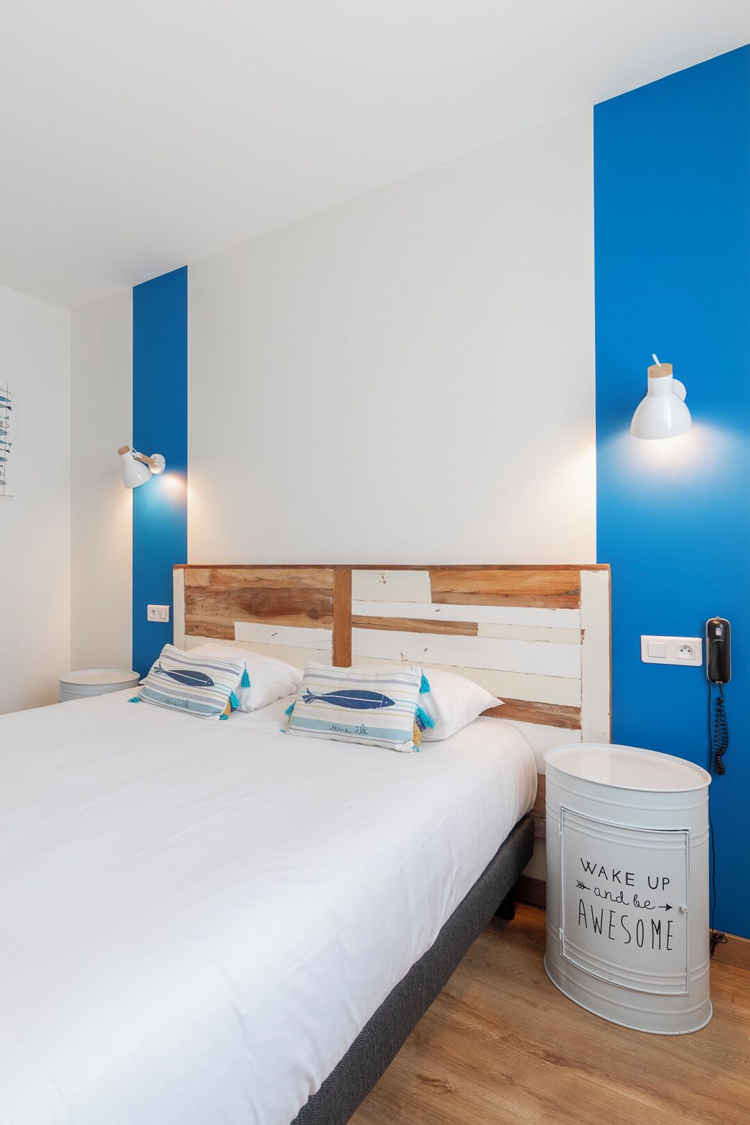 A modern bedroom with a wooden headboard, white bedding, and a blue accent wall.