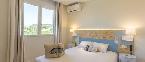 A bedroom with a bed, curtains, an air conditioning unit, a nightstand, and a wall-mounted lamp.