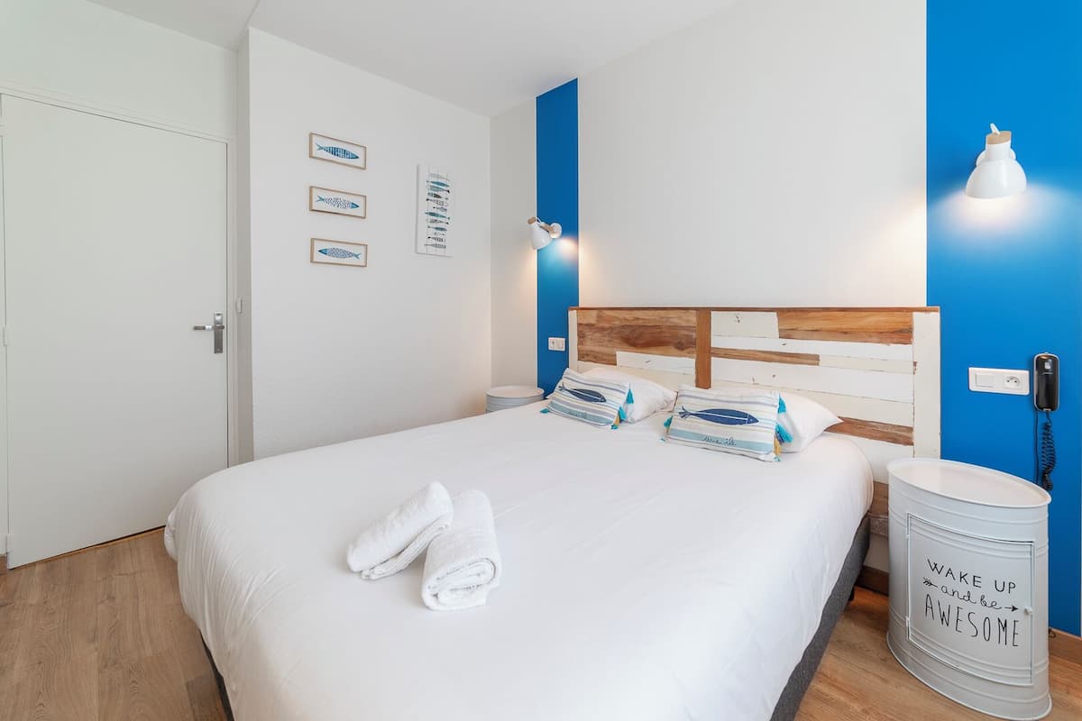 A neatly made bed with white linens and two rolled towels, a wooden headboard, and a wall with framed fish illustrations.